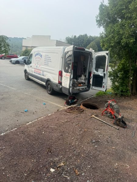 The van with its rear doors open and drain cleaning equipment unloaded onto the ground beside it.