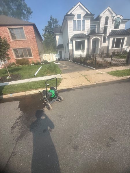 Drain cleaning equipment set up at the kerb outside a large house on a residential street.