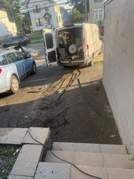 Paving slabs lifted and stacked beside a house to reach the drain line underneath, with the van parked alongside.