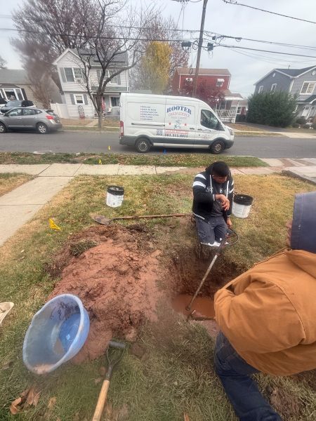 Two technicians working in an excavation in a front lawn, with buckets and a shovel alongside and the van at the kerb.