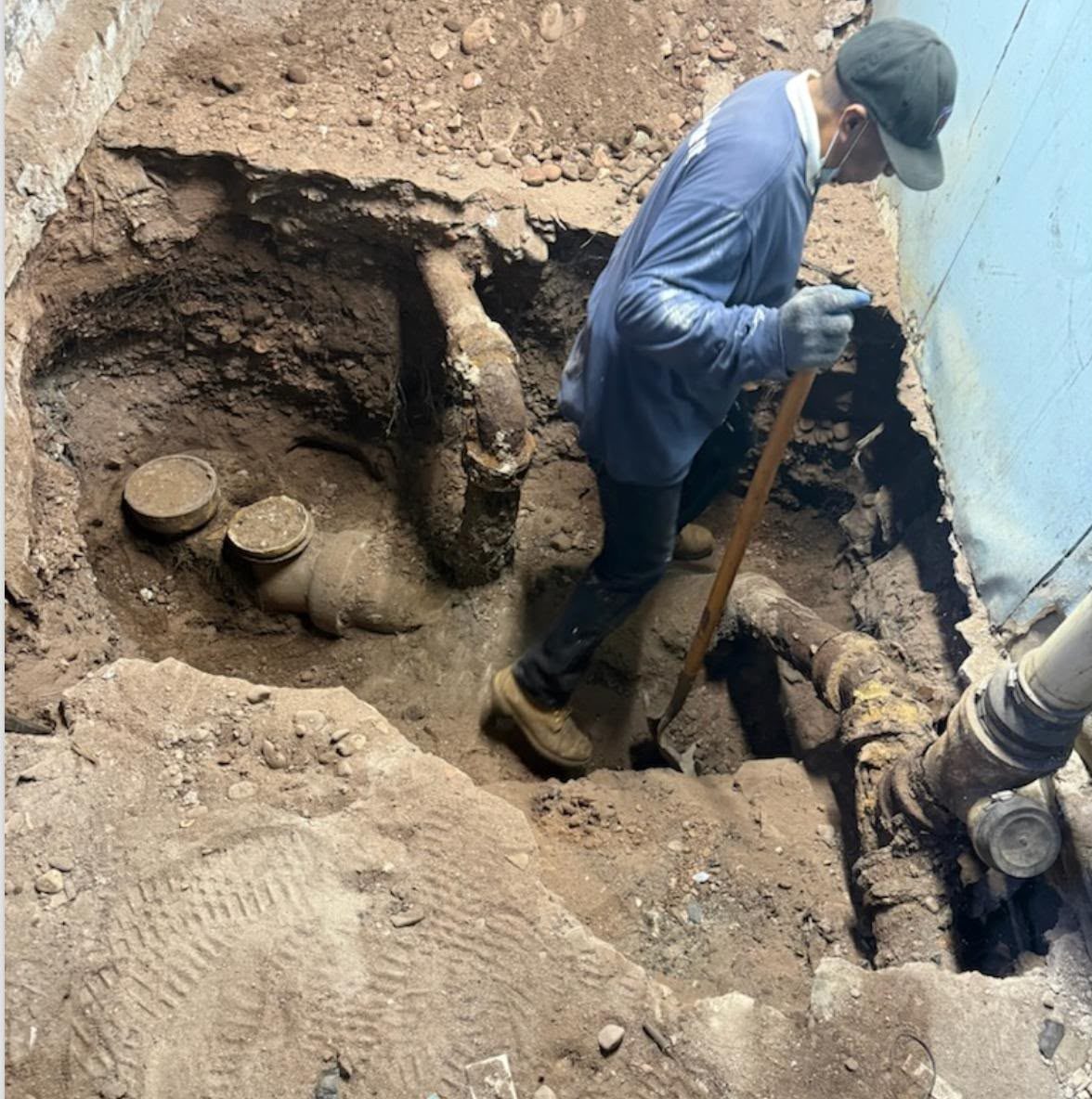 A technician standing in an open excavation, working on a pipe at the bottom of the hole.